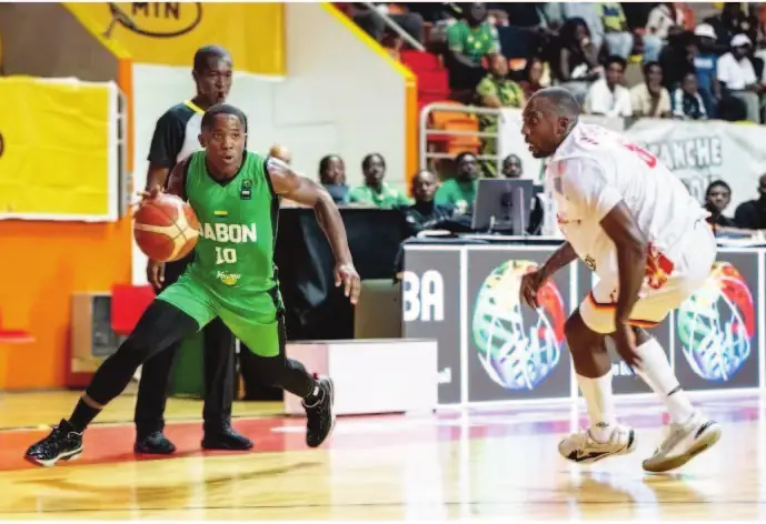 Un basketteur gabonais, maillot vert numéro 10, conduit le ballon face à un défenseur camerounais.