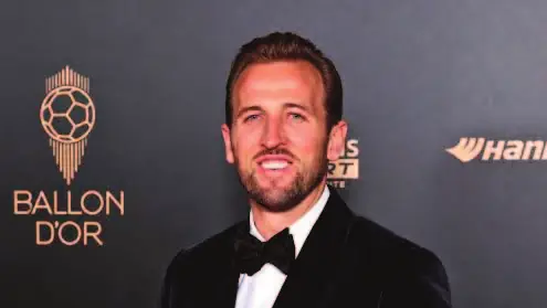 Harry Kane pose avec le Ballon d’or devant le panneau de la cérémonie.