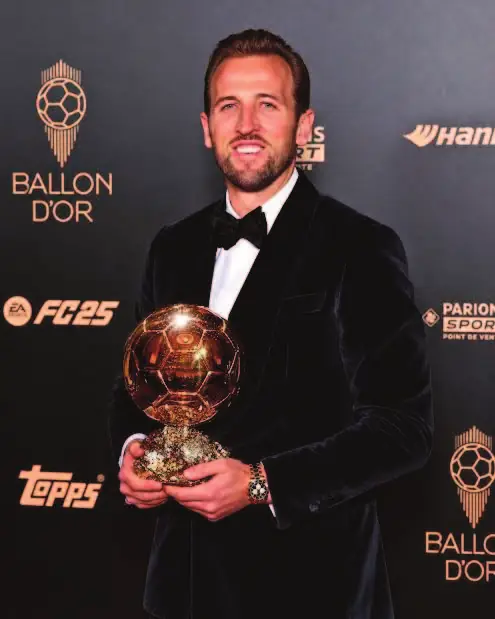 Harry Kane pose avec le Ballon d’or devant le panneau de la cérémonie.