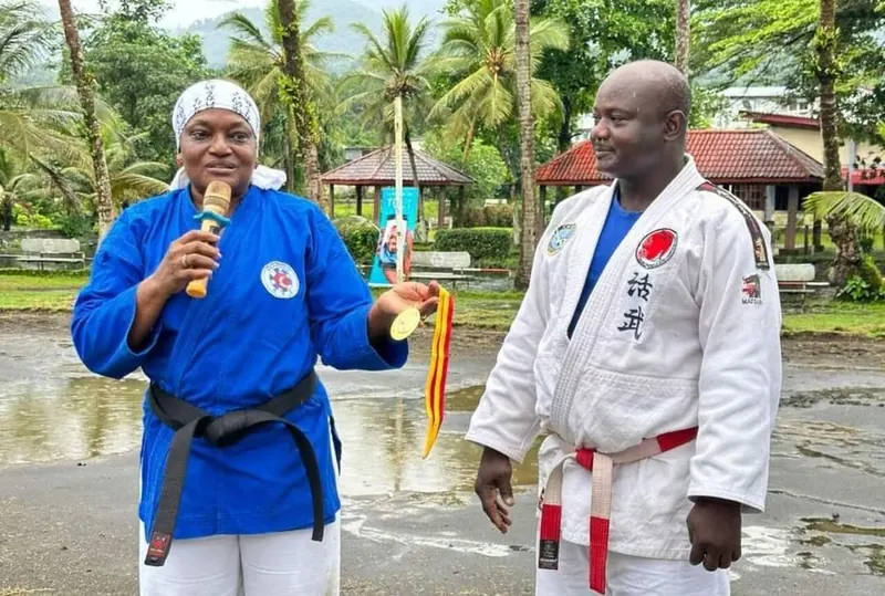Une nanbudoka camerounaise en kimono bleu, micro en main, aux côtés d’un maître en kimono blanc.