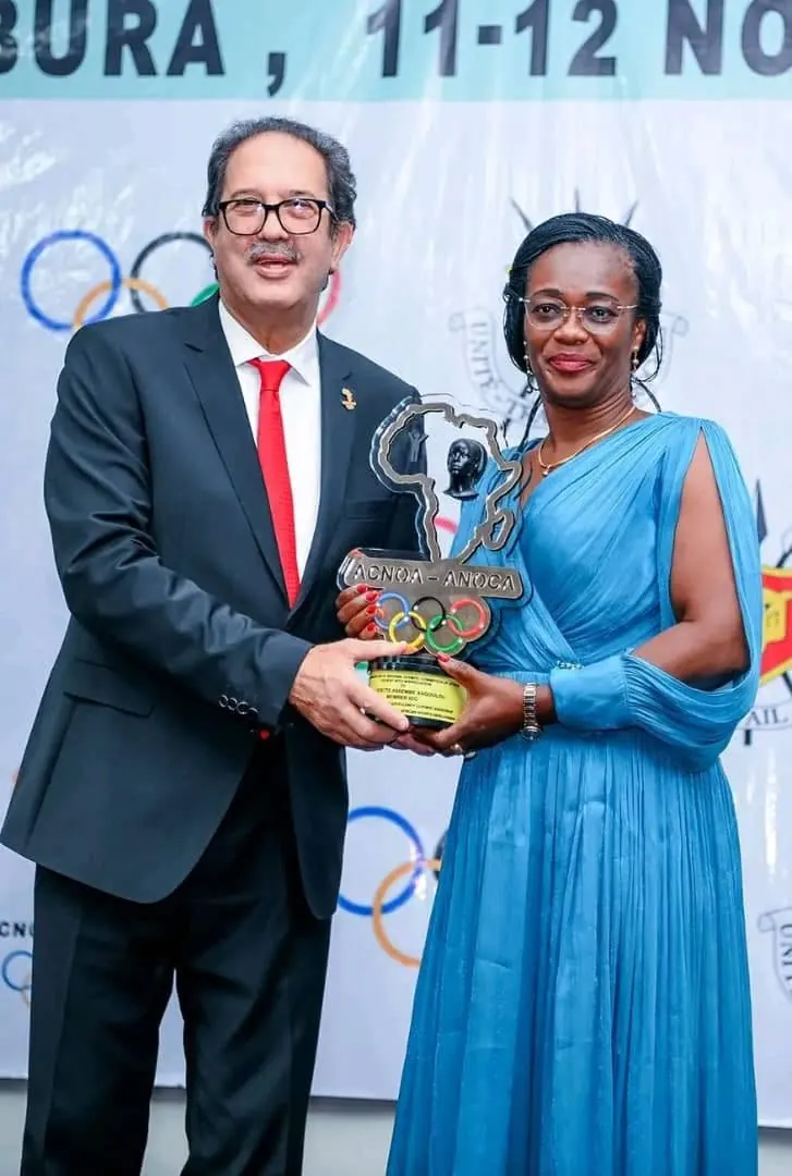Célestine Odette Assembé Engoulou, en robe bleue, reçoit un trophée devant le logo des anneaux olympiques.
