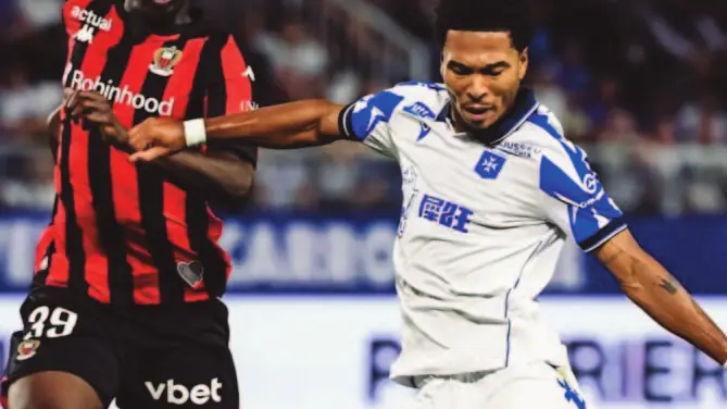Un joueur rennais en maillot rouge et noir à la lutte avec un joueur d’Auxerre en blanc.